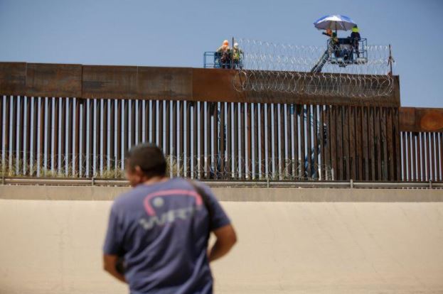 عمال أمريكيون يضعون أسلاكا شائكة على سياج حدودي على الحدود الأمريكية مع المكسيك. تصوير: خوسيه لويس جونزاليز - رويترز.